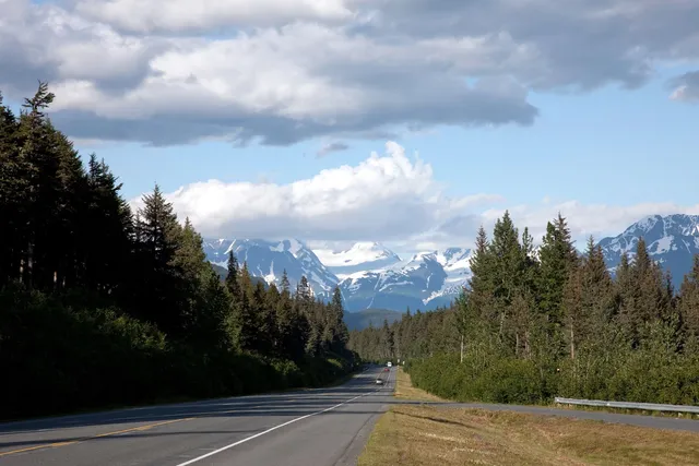 Seward Highway in Alaska running through forest toward snowy mountains