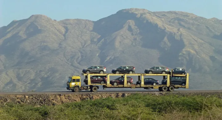 Loaded car carrier truck crossing open country below a mountain range