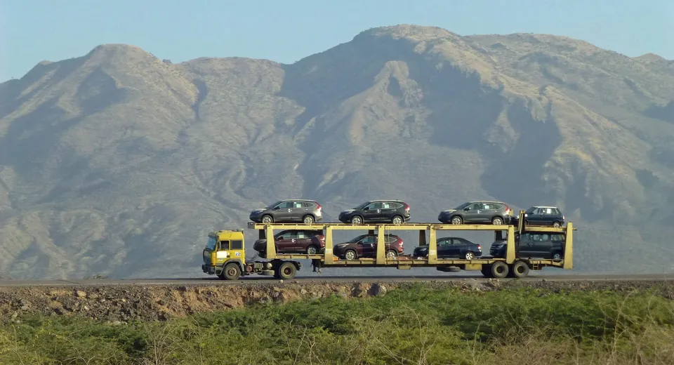 Loaded car carrier truck crossing open country below a mountain range