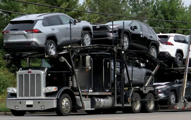 Open car carrier truck loaded with SUVs on a two-lane road