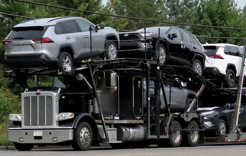 Open car carrier truck loaded with SUVs on a two-lane road