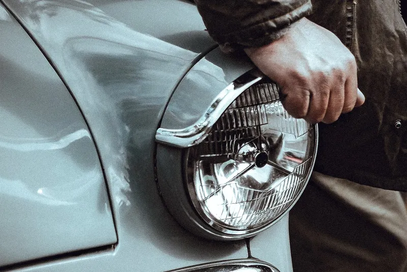 Hand on the headlight and fender of a classic car