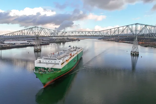 Car carrier ship sailing under a steel bridge