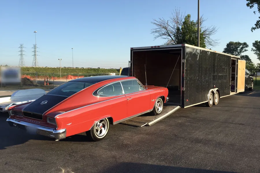 Classic car parked beside an enclosed car trailer with its ramp open
