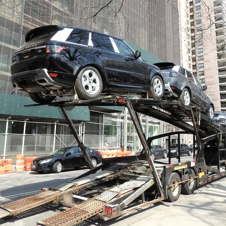 SUVs strapped to the deck of an open car carrier with the loading ramps down