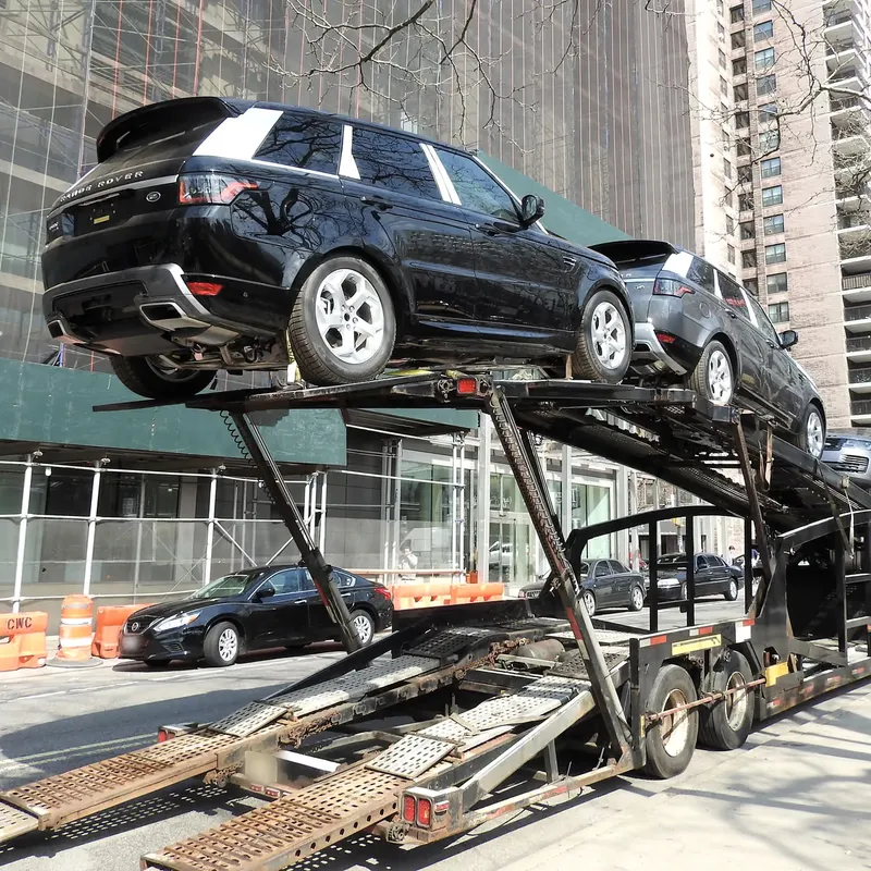 SUVs strapped to the deck of an open car carrier with the loading ramps down