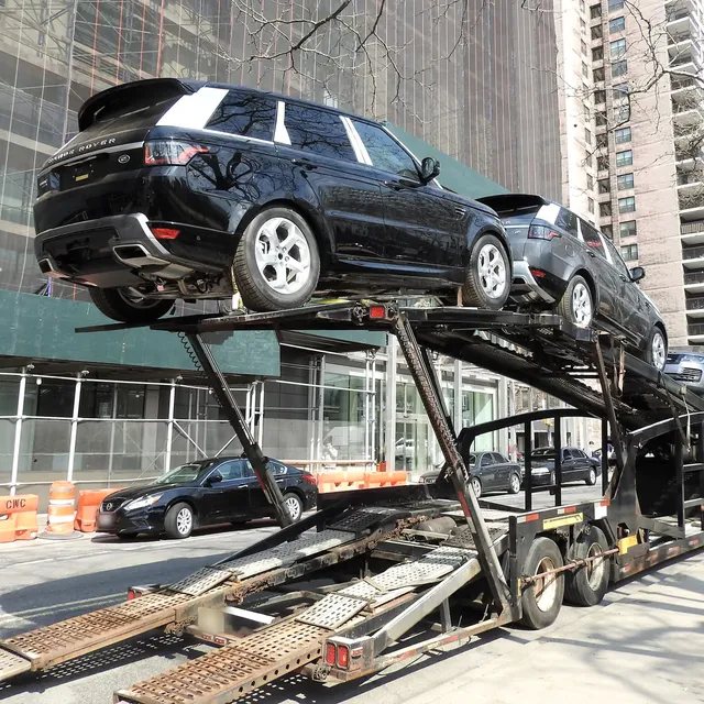 SUVs strapped to the deck of an open car carrier with the loading ramps down